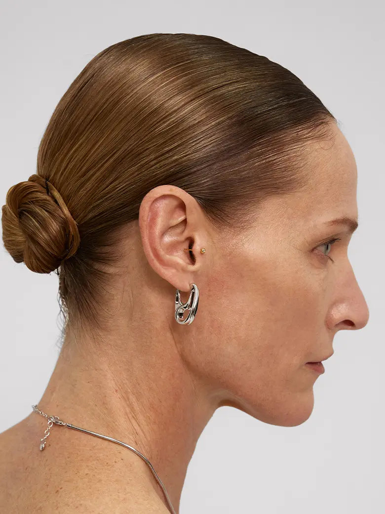 Woman wearing Contour Silver Hoops Earrings, showcasing minimalist sculptural design with smooth curves.