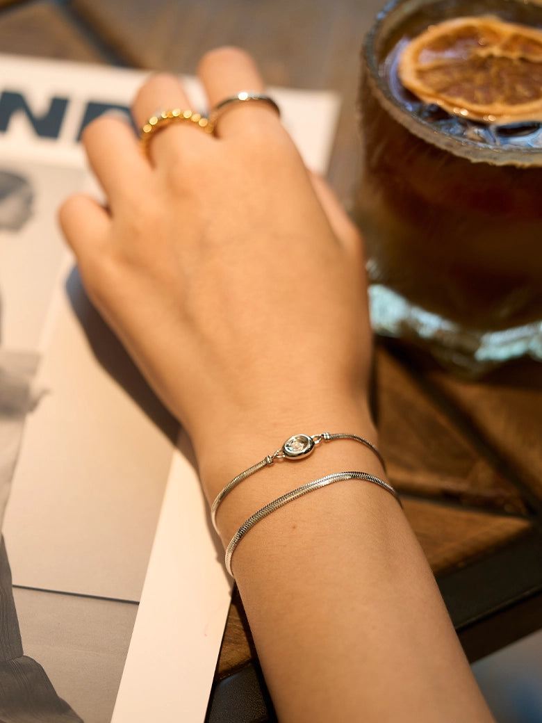 A hand wearing a Flat Snake Silver Bracelet alongside a drink, showcasing its sleek design and versatility.