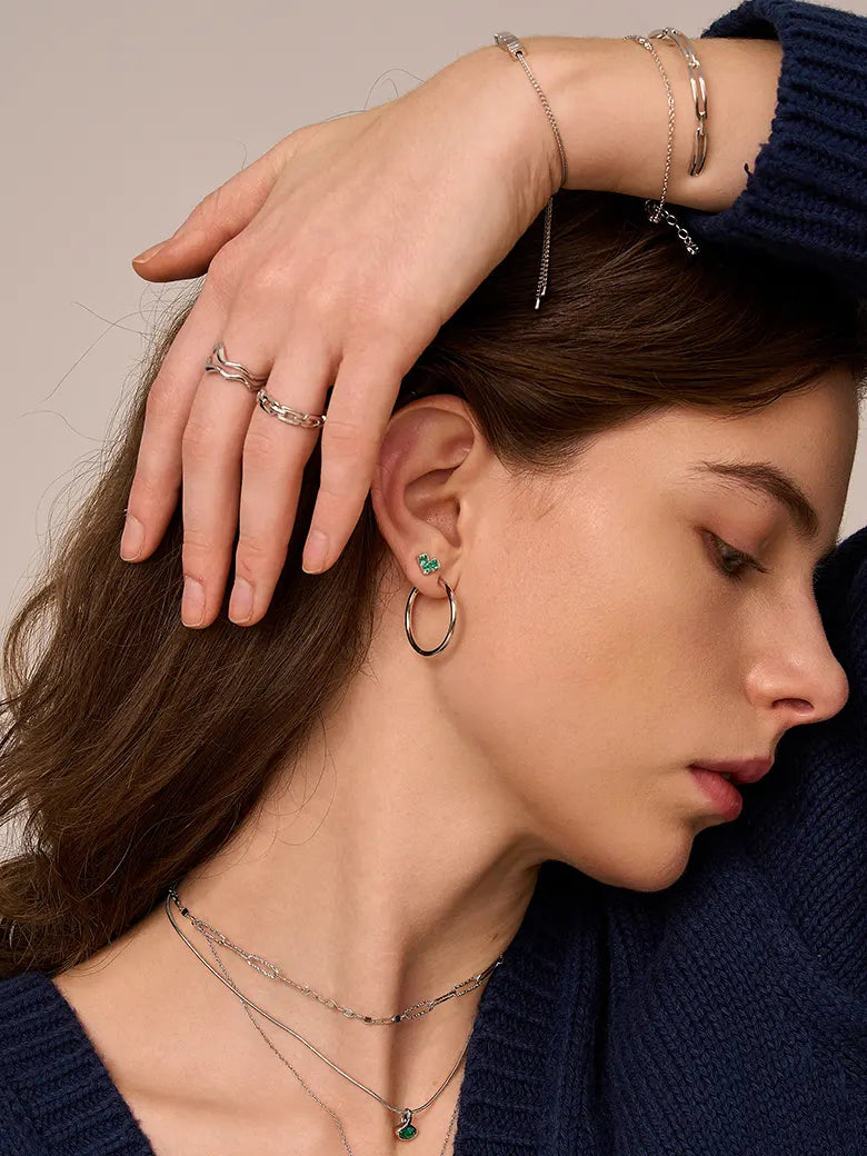 Close-up of a woman's ear showcasing PrincessCutEmeraldHeartSilverHoopEarrings