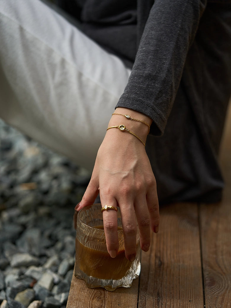 A close-up of a hand wearing a Solitaire Snake Chain Bracelet while holding a glass, showcasing elegance and style.